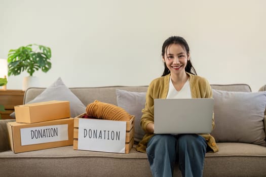 Woman asian holding donation box full with clothes and select clothes. Concept of donation and clothes recycling. Helping poor people.