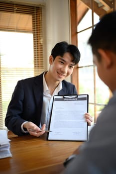 Friendly male insurance agent in suit pointing at contract document to client put a signature.