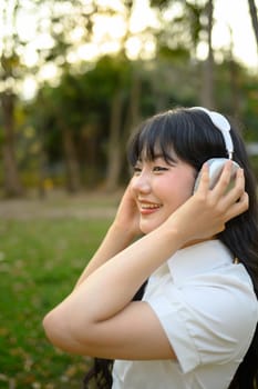 Portrait of young woman enjoying the music in headphone while standing in the park.
