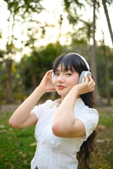 Attractive young woman listening music with headphones, relaxing in the park.
