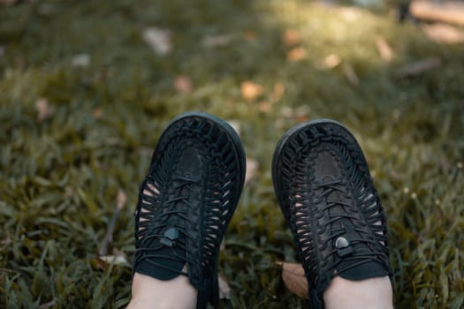 Close up male feet in sneakers on green lawn dappled with sunlight.