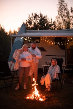 The family is relaxing together by the campfire near their mobile home. Evening family vacation.