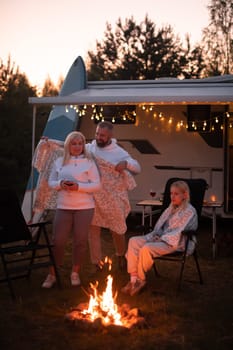 The family is relaxing together by the campfire near their mobile home. Evening family vacation.