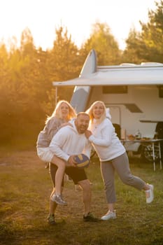 Happy parents with their child playing with a ball near their mobile home in the woods.