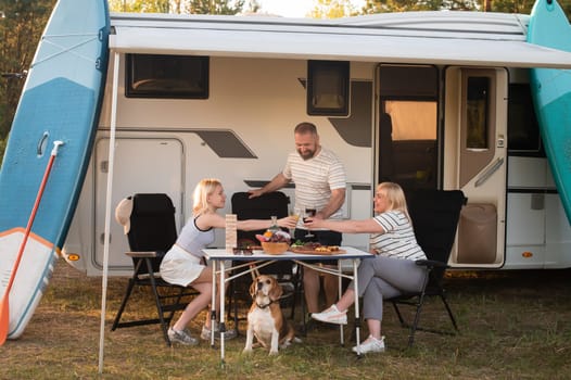 A happy family is resting nearby near their motorhome in the forest.