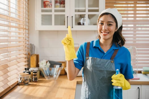 Young woman in apron and rubber glove ready for house cleaning. Promoting hygiene and housekeeping with spray bottle in hand. Clean disinfect home care. maid with liquid.