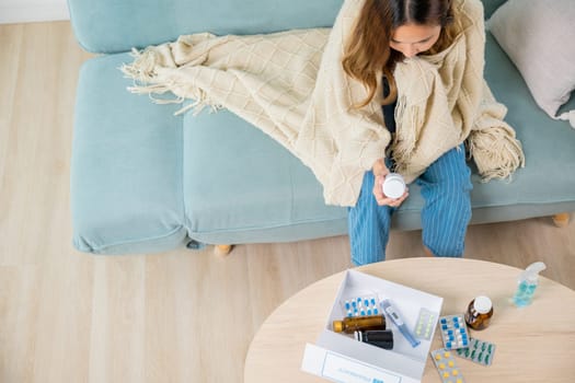 Asian young woman reading ingredient and hold bottle of drug on sofa at home, sick people reading information medicine label pills, female with flu virus, Health care and medicine concept