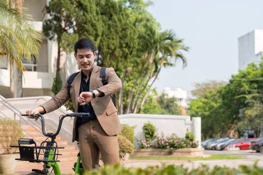 Asian businessman in a suit is riding a bicycle on the city streets for his morning commute to work. Eco transportation concept, sustainable lifestyle concept.