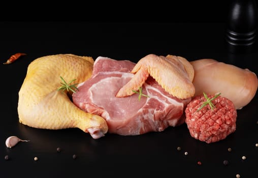 Different types of raw meat - beef, pork, chicken on a black wooden board,
