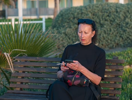 a woman with a cigarette and a phone sits on a bench near the Mediterranean Sea 1