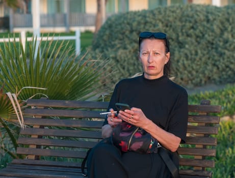 a woman with a cigarette and a phone sits on a bench near the Mediterranean Sea 3