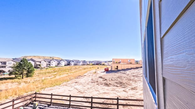 Denver, Colorado, USA-August 30, 2023-New residential neighborhood reveals the stark contrast between the raw wooden frame of an under-construction building and the completed homes in the background, with vehicles and building materials dotted across the landscape under a vast blue sky with fluffy clouds.