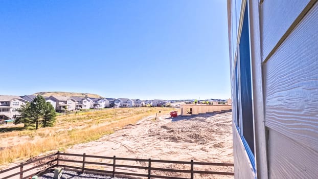 Denver, Colorado, USA-August 30, 2023-New residential neighborhood reveals the stark contrast between the raw wooden frame of an under-construction building and the completed homes in the background, with vehicles and building materials dotted across the landscape under a vast blue sky with fluffy clouds.