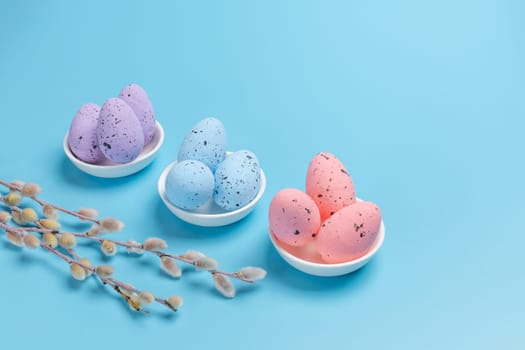 Porcelain saucers with colored Easter eggs and willow branches with catkins on the blue background. Top view.