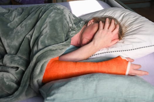 woman with a broken right arm with an orange fiberglass plaster cast sleeps in bed with a pillow under the cast, everyday life with trauma, High quality photo