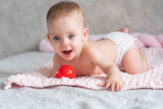 A baby cuddles a red ball while lying on a blanket.