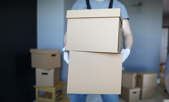 Close-up of male carrying cardboard boxes in gloves. Delivery service. Unpacked personal things in cartons. Moving day and new property. Renovation and handyman concept