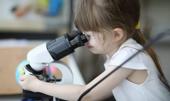 Close-up of cute child investigating sample under microscope. Kid having fun with research indoors. Spare time with exploration. Funny science and childhood concept