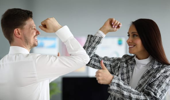 Portrait of cheerful male and female competing whos stronger. Co-workers showing thumbs up. People in luxury suits. Business company and fun on working place concept