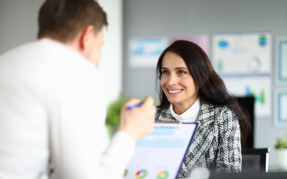 Close-up of cheerful office worker talking to co-worker. Brunette lady with shining smile and luxury costume. Happy young woman discussing working moment. Business company concept