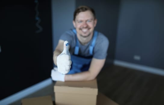 Close-up of smiling man showing thumbs-up. Cheerful male worker in empty room with carton. Well done and good job. Renovation and change interior design concept