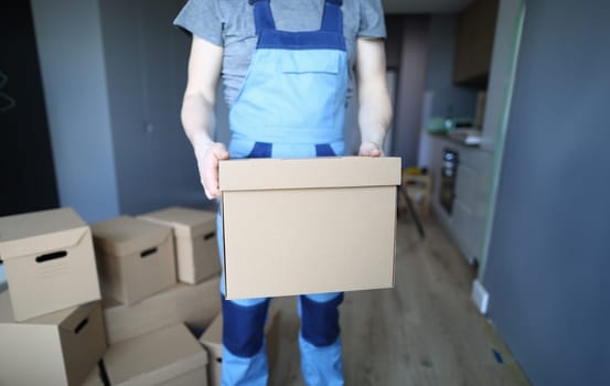 Close-up of worker hands holding empty cardboard box. Professional carpenter or foreman. Room full with cartons. Interior designer and renovation in new apartment concept