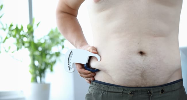 Close-up of male hand holding special metering fitness utility using to look at overweight belly. Fat man preparing for training. Severe obesity and losing weight concept