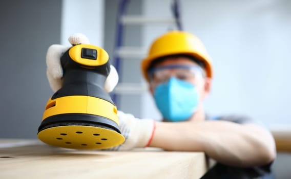 Masked builder polishes sander wooden surface. Rotational and oscillatory movements equipment. Electrical technology, creates comfortable repair conditions. Man polishes and grinds surfaces