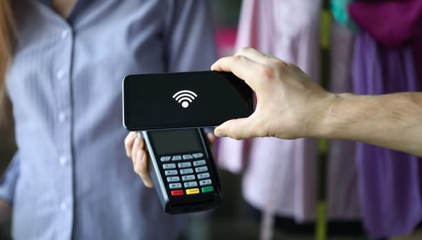 Close-up of people hands holding terminal for payments and smartphone with connection sign on screen. Fast pay bills. Contactless method and modern technology concept
