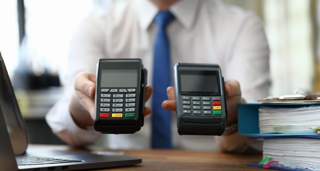 Close-up of person hands holding two different terminals for contactless payment. Seller proposing for choice various variants. Modern technology concept