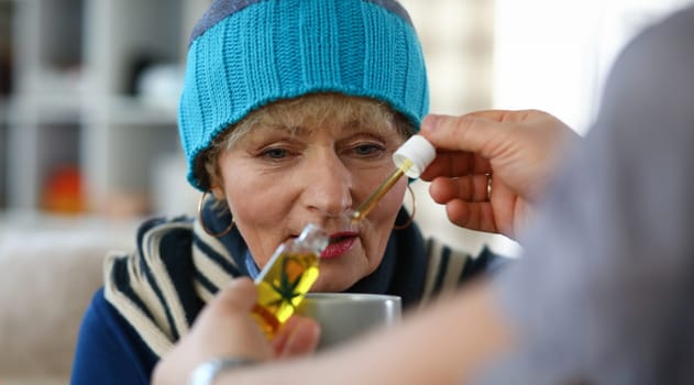 Close-up of unhealthy grandma holding cup with medication. Hand of male person adding cannabinoid oil to bowl of sick granny. Sickness and treatment concept