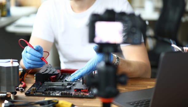 Close-up view of person measuring voltage using voltmeter and filming it on videocamera. Male recording video for vlog. Beginner vlogger or hobby for repairman concept