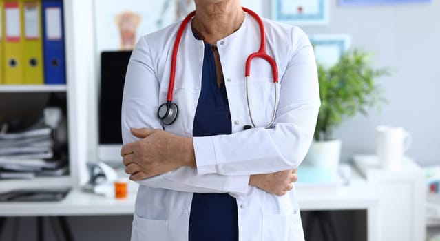 Close-up of elderly woman working in hospital. Lady with folded hands. Experienced doctor using special medical equipments. Health care and prevention concept