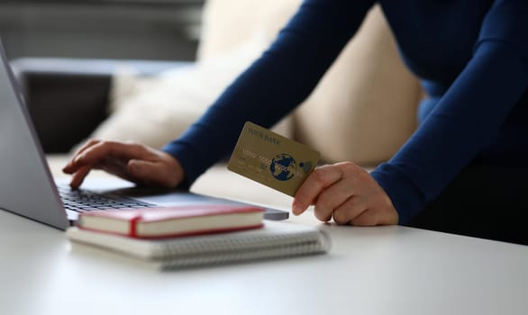 Close-up of woman making payment via internet on laptop. Female holding plastic credit card. Notebook on desktop. Online shopping and modern technology concept