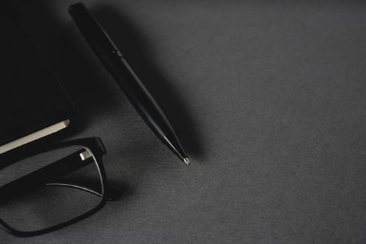 Top view of ballpoint pen, glasses and notepad lying on dark gray table