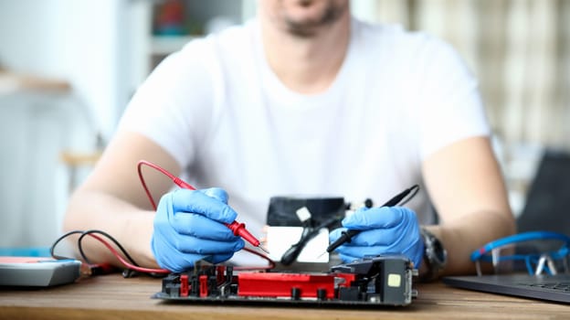 Close-up of male wearing protective blue gloves and using voltmeter on repairing detail. Middle-aged man measuring voltage. Technology and diy concept