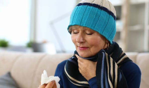 Close-up of ill elderly woman blowing nose in paper scarves. Unhealthy granny on sick leave. Female person taking medication. Sickness and treatment concept