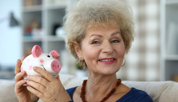 Portrait of elderly female holding piggy-bank and smiling on camera. Perfect method for planning budget and saving money for future. Investment and income concept