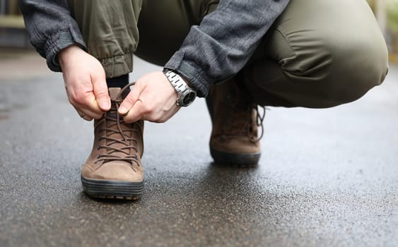 Close-up view of male hands sitting down outside on street and tying shoelaces on sneakers. Person lacing up stylish shoes. Sport walking and running concept