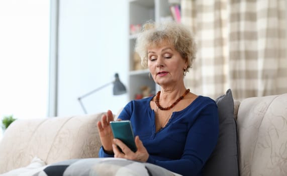 Portrait of senior woman using mobile phone. Attractive elderly female goes with the times. Copy space in left side. Cozy living room interior. Technology concept