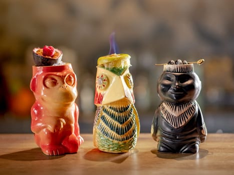 Tiki Drink Cocktails Collection. Set of three tropical tiki cocktails on bar counter. Beautiful tiki cocktails, different decorated with fire flame on bar in night club