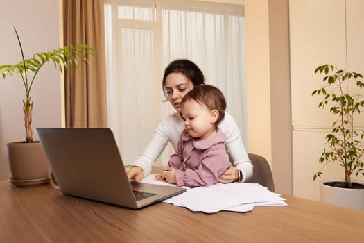 Cheerful pretty businesswoman working at home with her little child girl