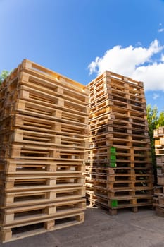 Piles of stacked natural wooden shipping pallets. Outside a big stack with big stack of wooden pallets.