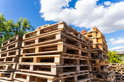 Piles of stacked natural wooden shipping pallets. Outside a big stack with big stack of wooden pallets.