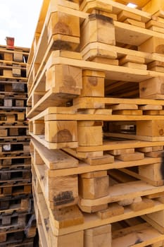 Piles of stacked natural wooden shipping pallets. Outside a big stack with big stack of wooden pallets.