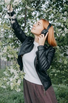 A red-haired teenage girl listens to music in headphones, configured via the phone. The time of spring flowering of cherry orchards