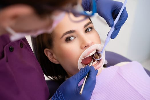 Dentist uses dental tools and mirror to check the teeth of woman patient.