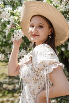 An attractive long-haired woman walks in the spring in the park of blooming apple trees. Spring portrait of a woman