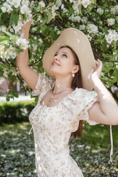 An attractive long-haired woman walks in the spring in the park of blooming apple trees. Spring portrait of a woman