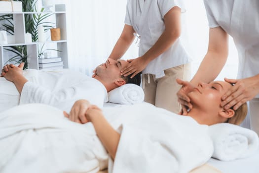 Caucasian couple enjoying relaxing anti-stress head massage and pampering facial beauty skin recreation leisure in dayspa modern light ambient at luxury resort or hotel spa salon. Quiescent